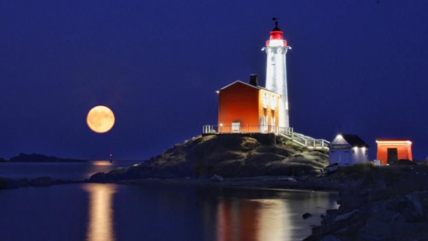 Fisgard Lighthouse at night. There is a setting full moon in the background.