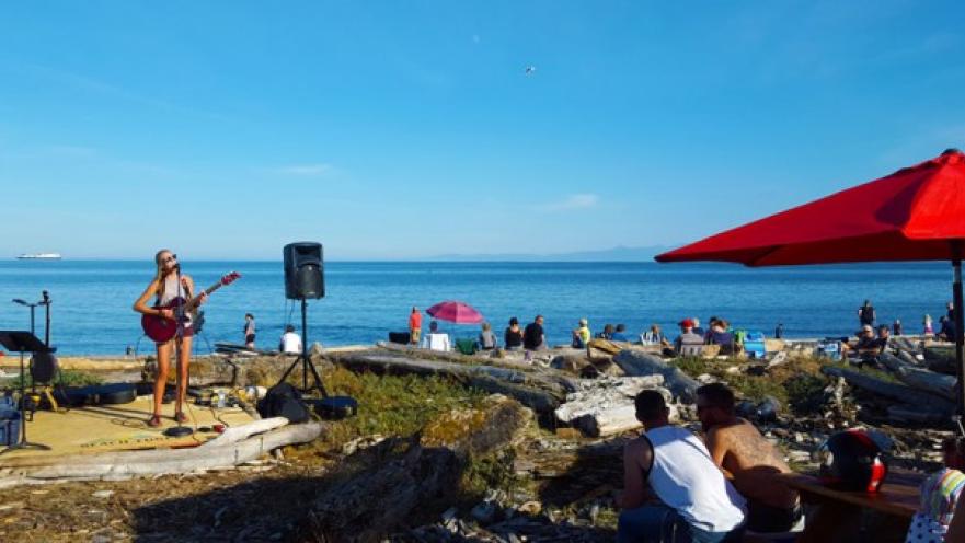 Performer playing guitar on stage near the beach. The day is sunny and the sky and ocean are blue.