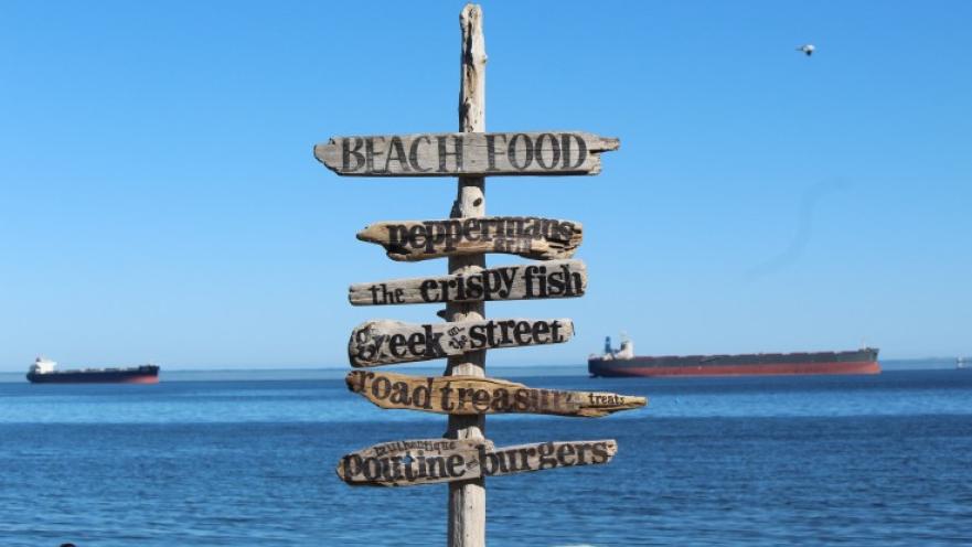 Wooden signage on beach indicating the different food places at the beach.