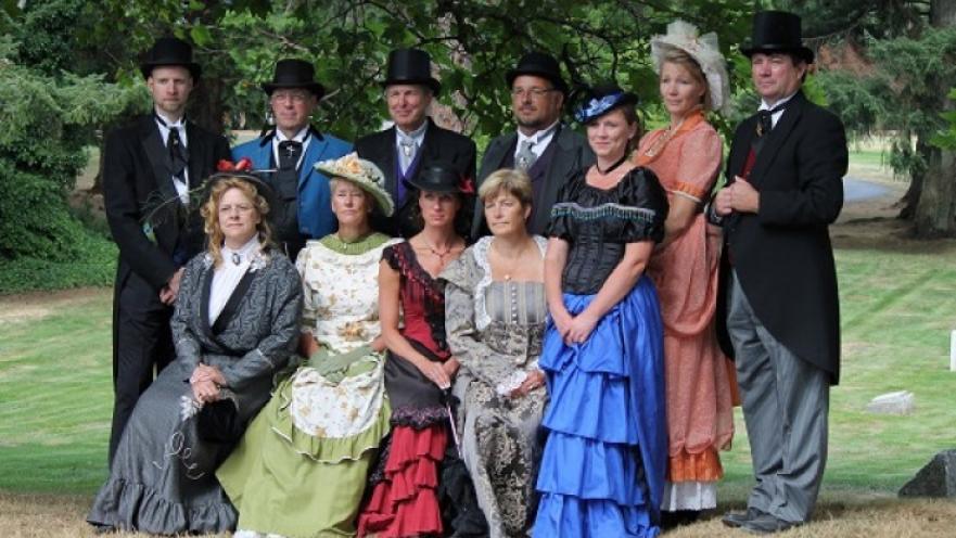 Group of men and women wearing old-timey clothing posing for a photo.