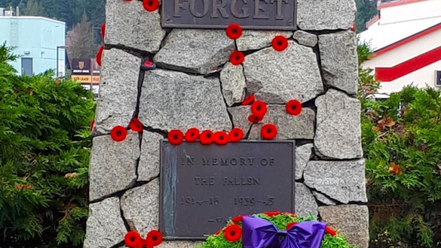 Lest we forget monument commemorating fallen soldiers. The monument has plaques with information and has been adorned with red poppy flowers.