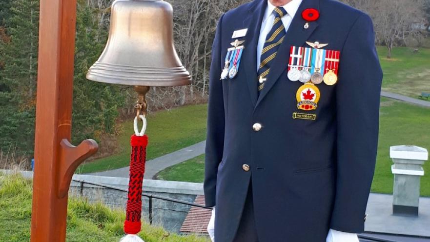Elderly veteran dressed in ceremonial armed forces uniform standing next to a bell..