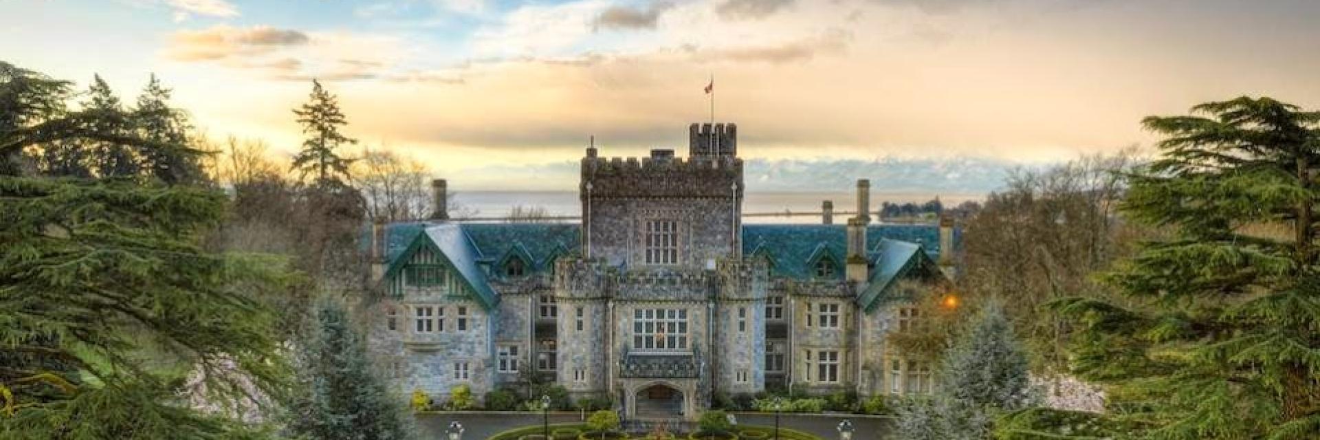 Grand historic Hatley castle with manicured gardens, surrounded by lush greenery and a dramatic sky in the background.