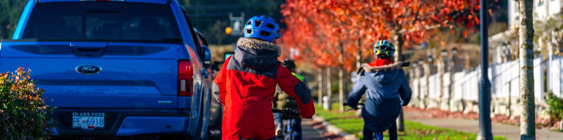 kids riding bicycles in a tree lined bike lane next to a truck 