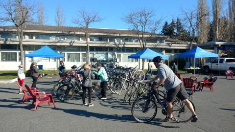Community event in Colwood with people checking and tuning bicycles under blue tents.