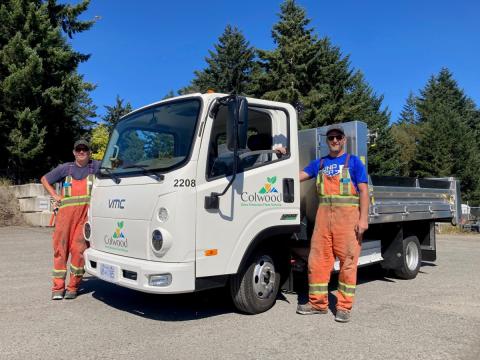 Two Colwood workers standing next to a white zero-emission fleet vehicle with the Colwood logo.