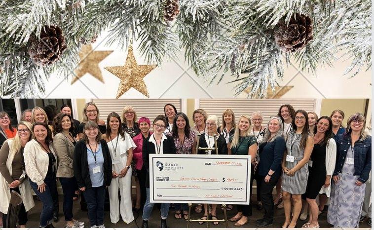 Group of women from the Women's Investing Network presenting a large check for $700, with a festive pine and star decoration above.