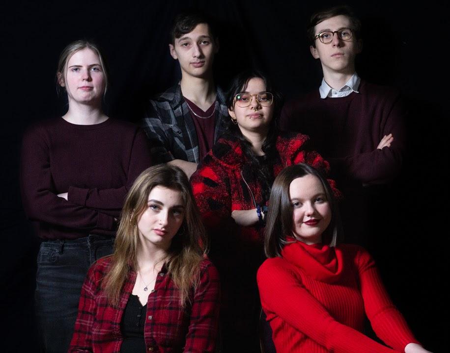 Group photo of six young people posing together against a black background.