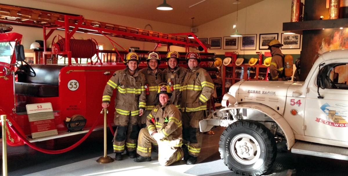 Group of firefighters posing inside a fire station with vintage fire trucks.